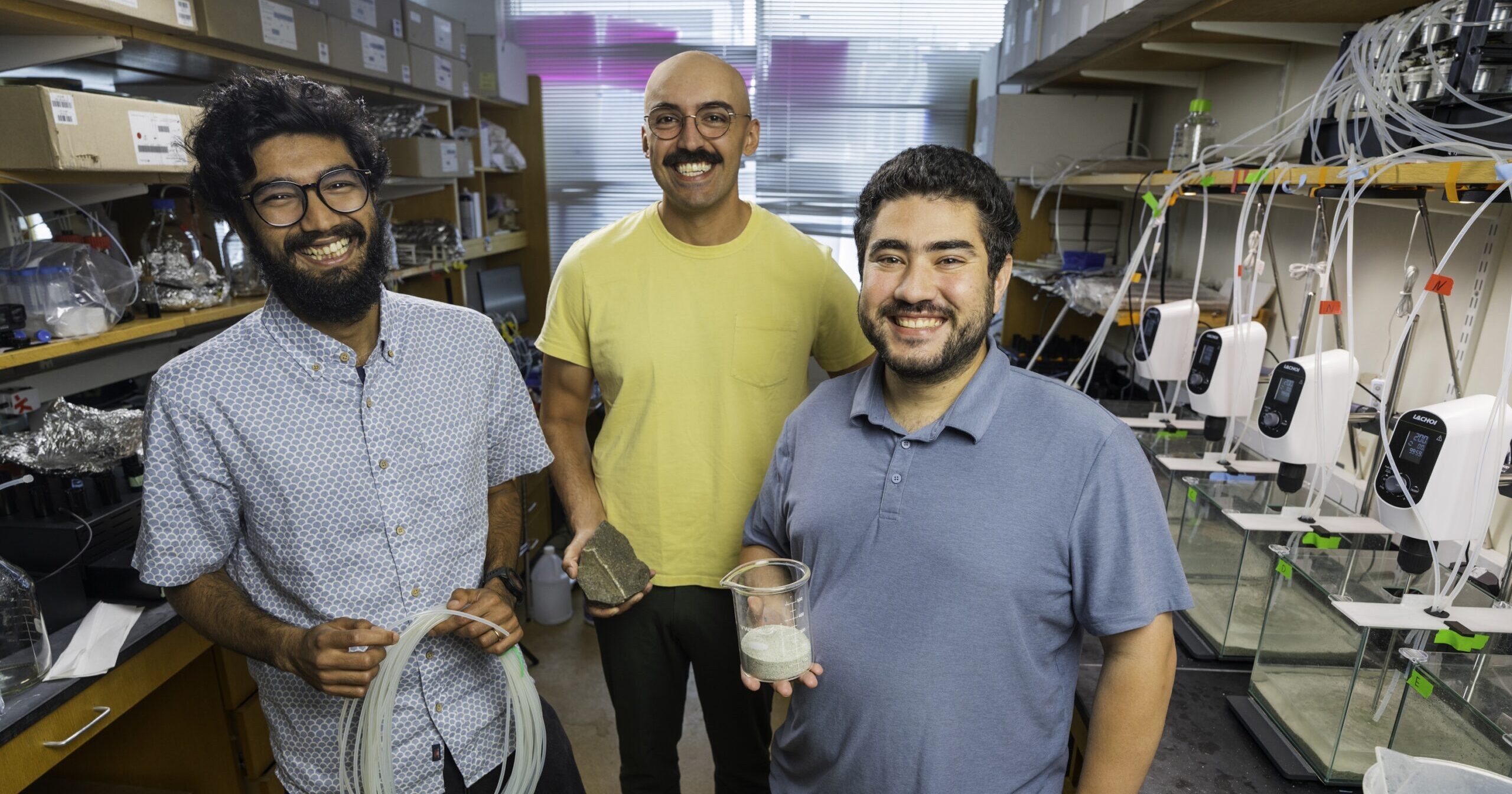 Three people in a lab, the one on the left is holding a long, thin tube, coiled together, the one in the center is holding a